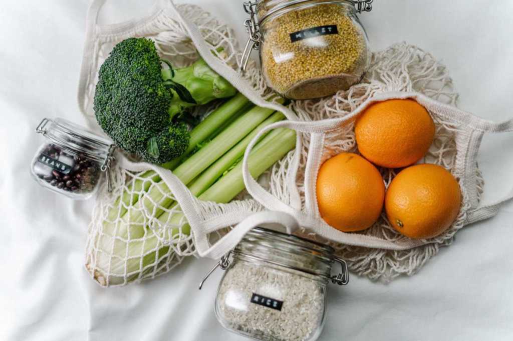 Fruit and vegetables in cloth shopping bags along with grains and rice in glass jars.