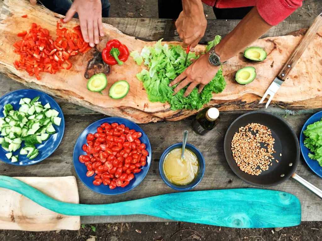 Two people cutting up vegetables for a meal outside.