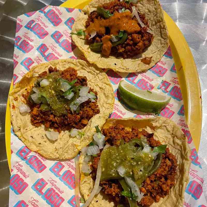 3 chorizo tacos on a yellow plate sitting on a metal table