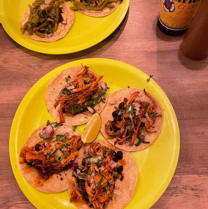Tacos on plates sitting on a wooden table with bottles of beer and salsa.